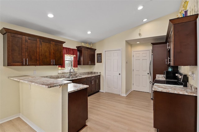 kitchen with a breakfast bar, sink, vaulted ceiling, light wood-type flooring, and kitchen peninsula