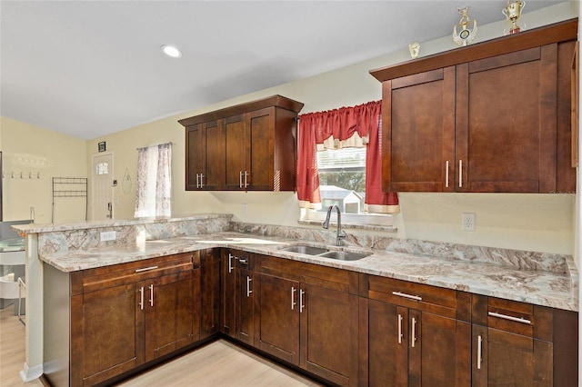 kitchen featuring light stone counters, sink, light hardwood / wood-style flooring, and kitchen peninsula