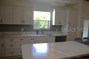 kitchen featuring a kitchen island, sink, a breakfast bar area, white cabinets, and black dishwasher