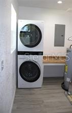 washroom featuring wood-type flooring, electric panel, and stacked washing maching and dryer