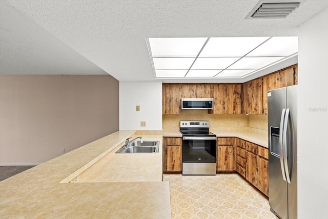 kitchen with sink, tasteful backsplash, a textured ceiling, appliances with stainless steel finishes, and kitchen peninsula