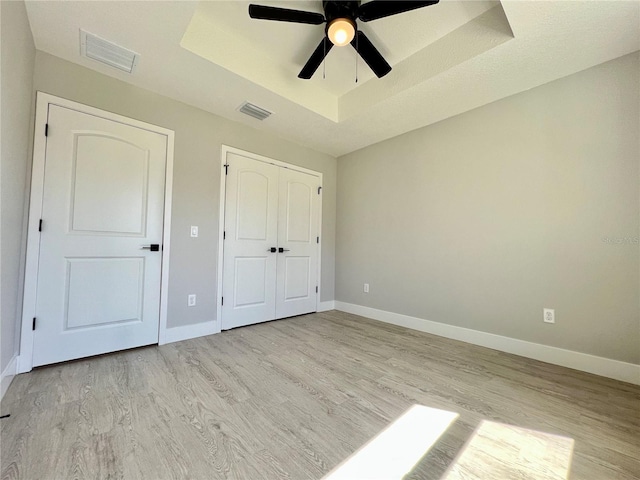 unfurnished bedroom featuring a raised ceiling, visible vents, light wood finished floors, and baseboards