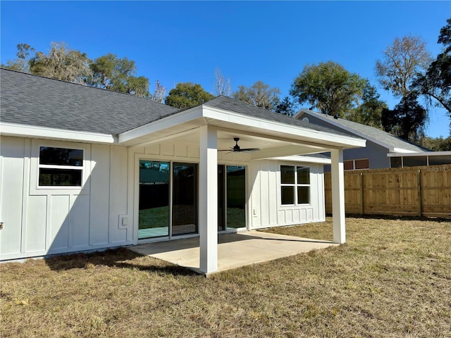 rear view of property featuring a shingled roof, a lawn, board and batten siding, fence, and ceiling fan