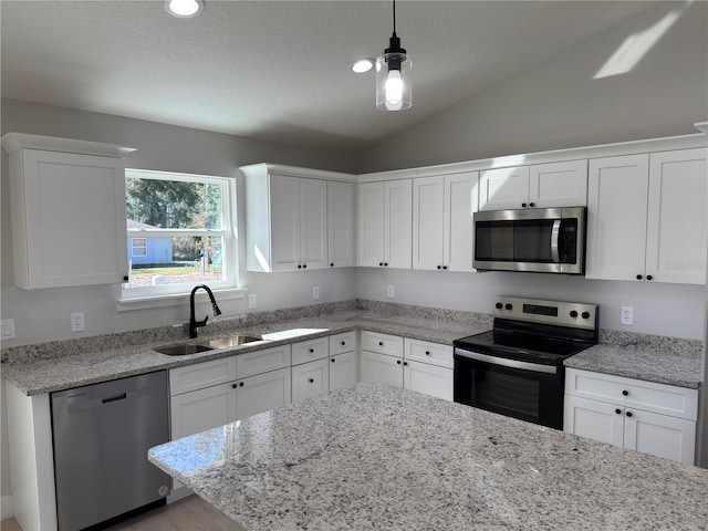 kitchen featuring lofted ceiling, a sink, white cabinetry, hanging light fixtures, and appliances with stainless steel finishes