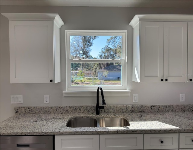 kitchen featuring stainless steel dishwasher, plenty of natural light, a sink, and white cabinetry