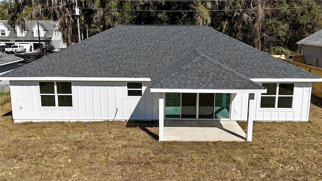 back of house featuring roof with shingles, a patio, board and batten siding, and a yard