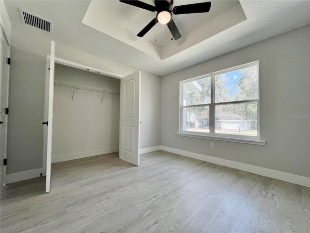 unfurnished bedroom with baseboards, visible vents, a tray ceiling, and wood finished floors