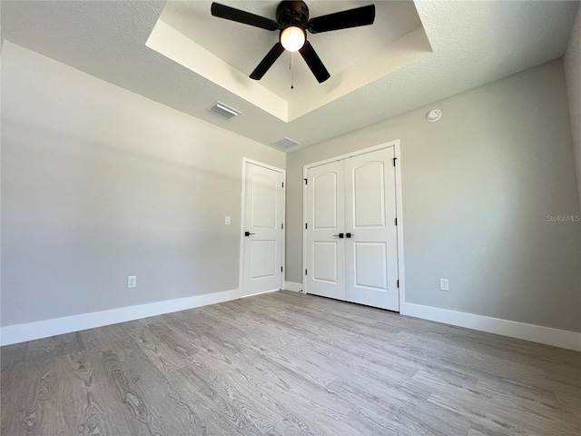 empty room with a raised ceiling, visible vents, baseboards, and wood finished floors