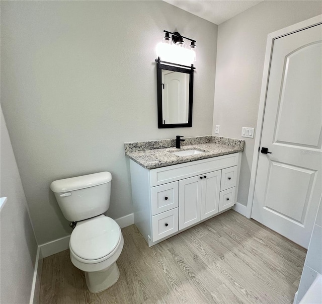 bathroom featuring toilet, wood finished floors, vanity, and baseboards