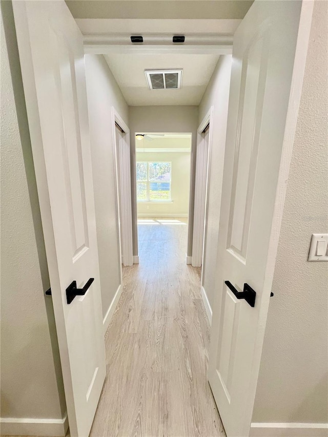 corridor with light wood-style floors, baseboards, and visible vents