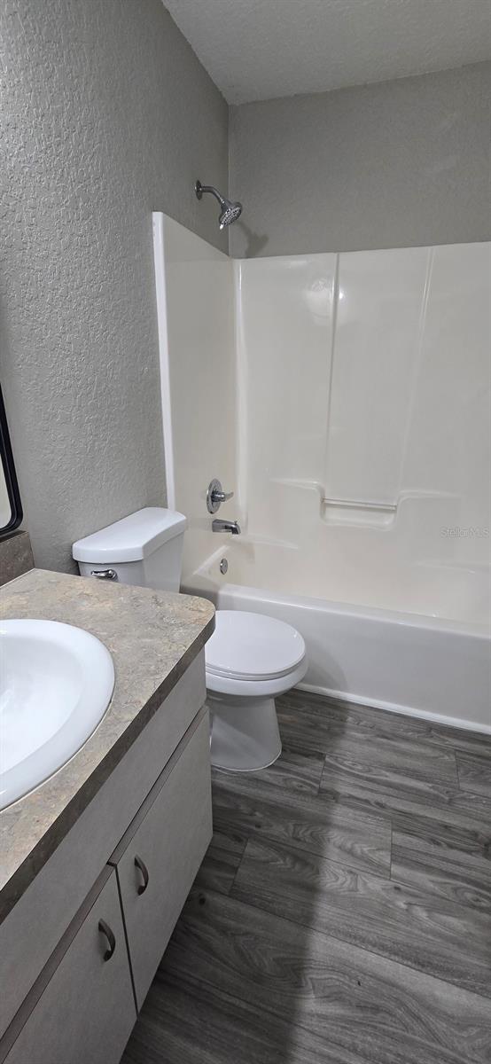 full bathroom featuring washtub / shower combination, toilet, wood-type flooring, a textured ceiling, and vanity