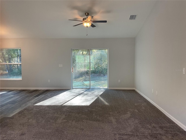 empty room featuring ceiling fan, plenty of natural light, and dark carpet