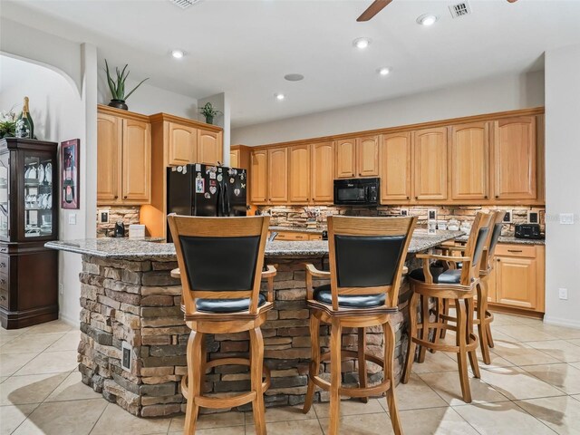 kitchen featuring a kitchen bar, light stone counters, black appliances, a kitchen island, and backsplash