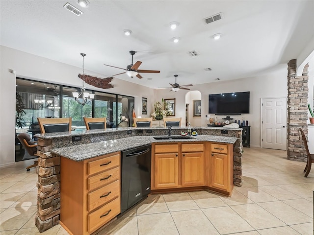 kitchen with light tile patterned flooring, sink, dark stone countertops, black dishwasher, and a kitchen island with sink