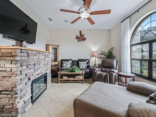 tiled living room with a stone fireplace and ceiling fan