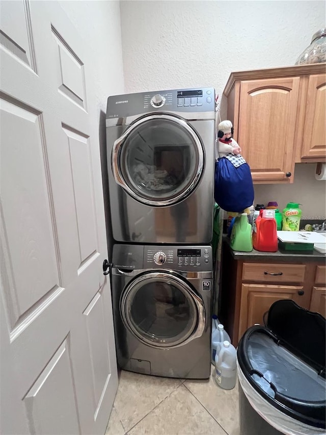 laundry area featuring cabinets, stacked washer / dryer, and light tile patterned floors