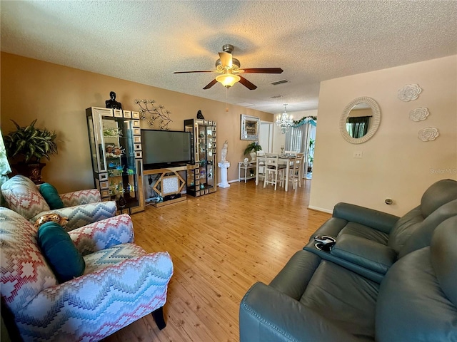 living area featuring baseboards, visible vents, a textured ceiling, light wood-style floors, and ceiling fan with notable chandelier