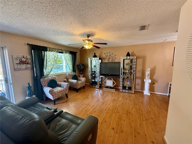 living room featuring light wood-style floors, ceiling fan, visible vents, and a textured ceiling