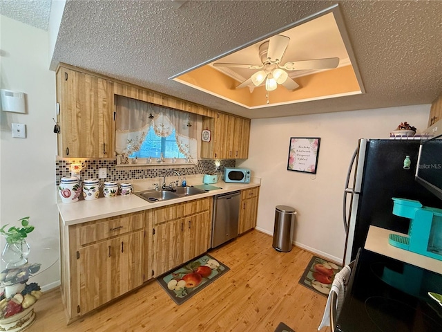 kitchen featuring stainless steel appliances, a sink, light countertops, light wood-type flooring, and a raised ceiling