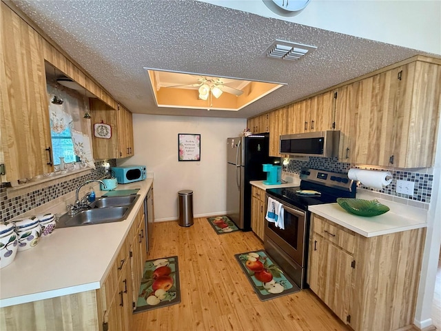 kitchen featuring a sink, appliances with stainless steel finishes, light countertops, and a tray ceiling