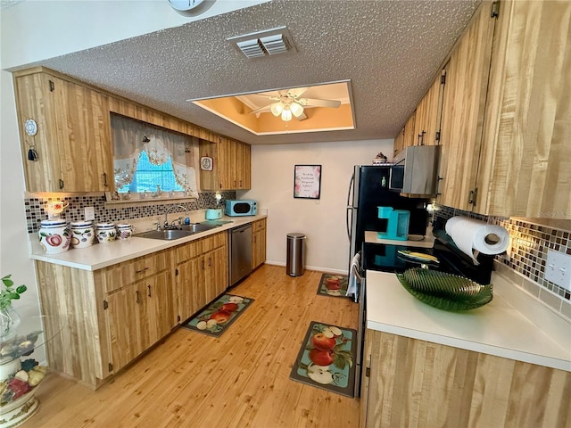 kitchen featuring a sink, light wood-style floors, dishwasher, a tray ceiling, and tasteful backsplash