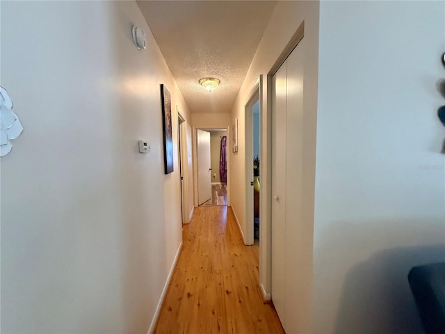 hallway featuring a textured ceiling, light wood-style flooring, and baseboards