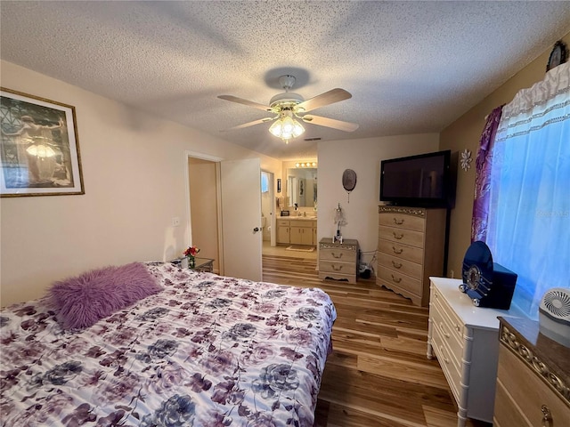 bedroom with a textured ceiling, ensuite bathroom, wood finished floors, visible vents, and a ceiling fan