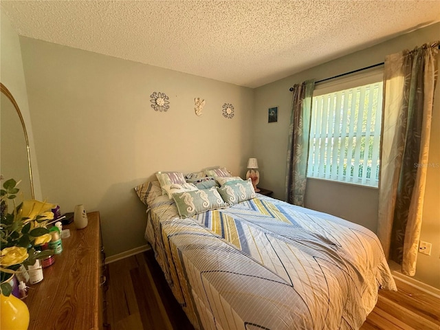 bedroom featuring a textured ceiling, baseboards, and wood finished floors