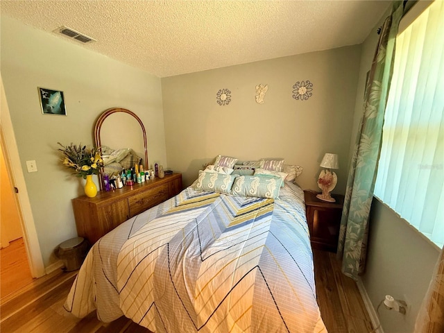 bedroom with visible vents, a textured ceiling, baseboards, and wood finished floors