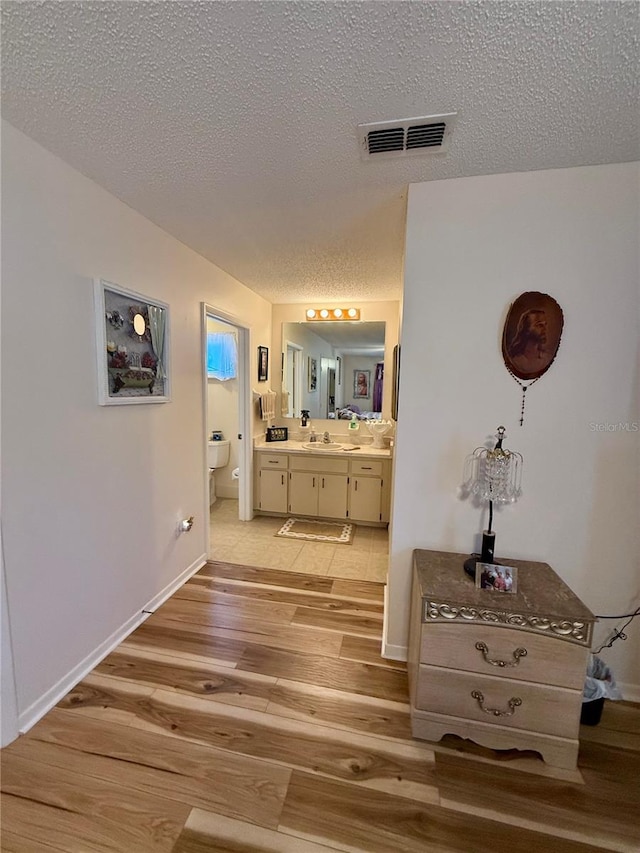 hallway with baseboards, visible vents, a textured ceiling, light wood-style floors, and a sink