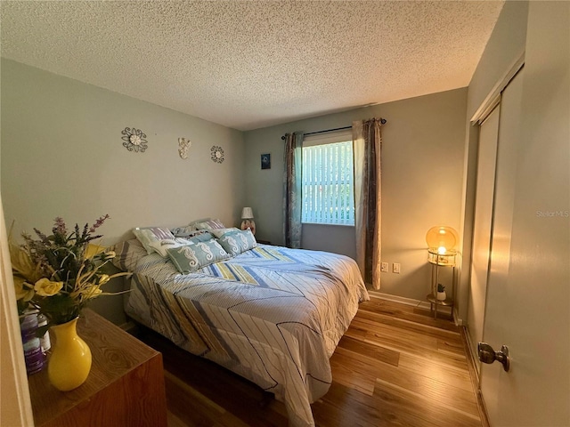 bedroom featuring a closet, a textured ceiling, baseboards, and wood finished floors