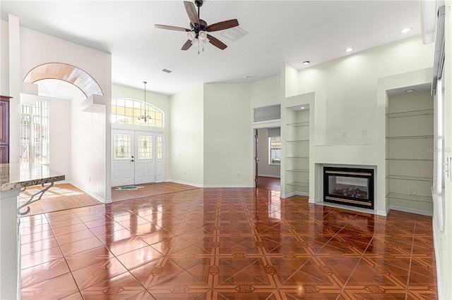 unfurnished living room with built in shelves, ceiling fan, and dark parquet floors