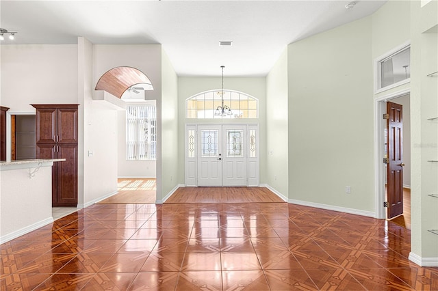 foyer entrance with an inviting chandelier, a towering ceiling, and dark parquet flooring