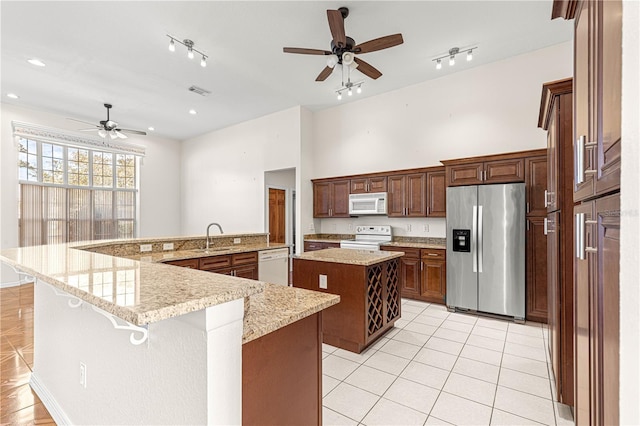 kitchen with sink, a breakfast bar area, light tile patterned floors, a large island with sink, and white appliances