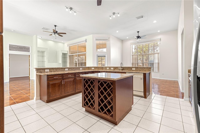 kitchen featuring light stone counters, dishwasher, a center island with sink, and light tile patterned floors