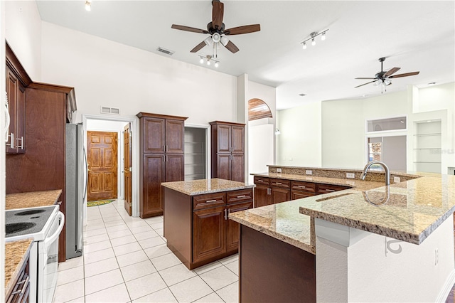 kitchen with sink, stainless steel fridge, white electric stove, a large island, and light stone countertops