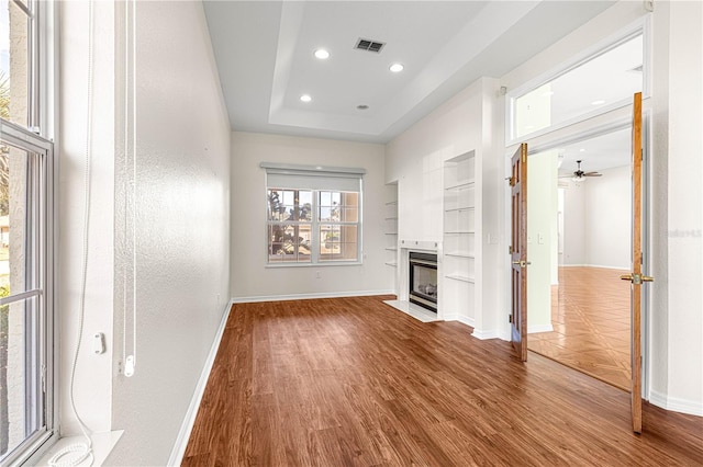 unfurnished living room featuring hardwood / wood-style flooring, a raised ceiling, ceiling fan, and built in shelves