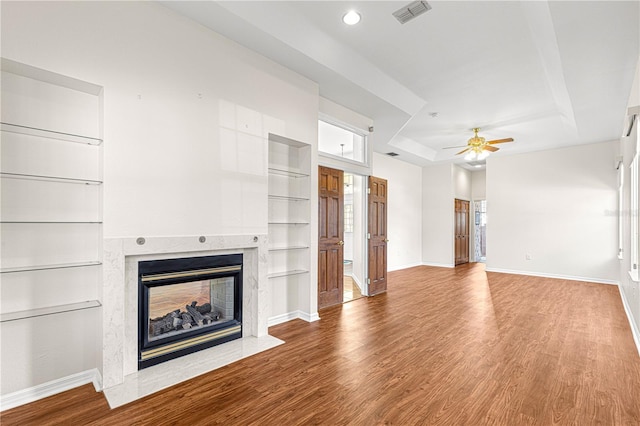 unfurnished living room featuring a tray ceiling, wood-type flooring, and a multi sided fireplace