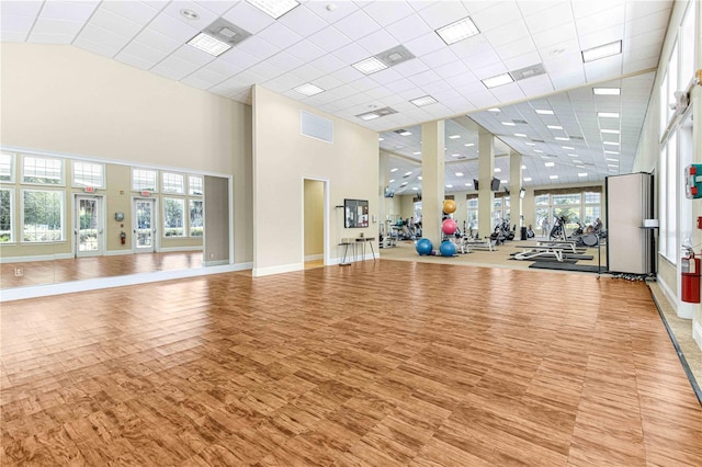 exercise room with a towering ceiling, a drop ceiling, and light wood-type flooring