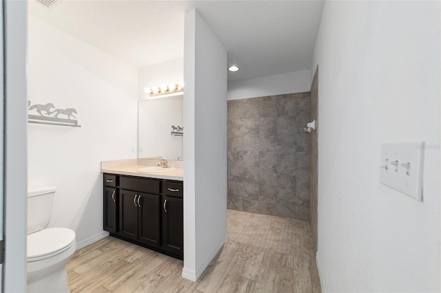 bathroom with vanity, toilet, hardwood / wood-style floors, and a tile shower