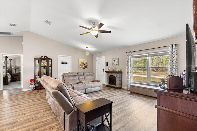 living room with ceiling fan, a stone fireplace, lofted ceiling, and light wood-type flooring