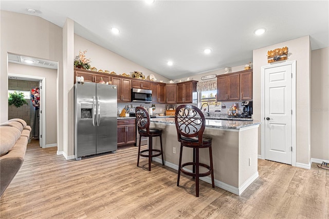 kitchen with a kitchen island, appliances with stainless steel finishes, a kitchen breakfast bar, light stone countertops, and light wood-type flooring