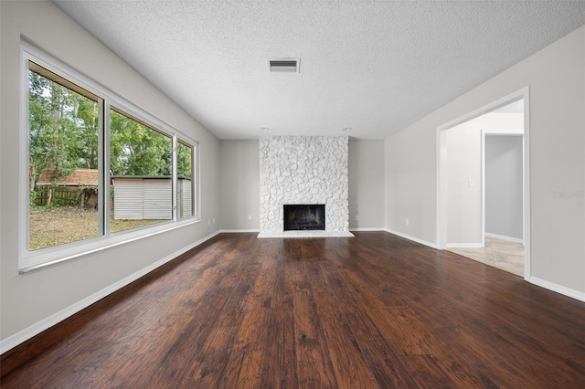 unfurnished living room with hardwood / wood-style flooring, a stone fireplace, and a textured ceiling