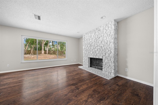 unfurnished living room featuring a stone fireplace, dark hardwood / wood-style floors, and a textured ceiling