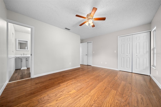 unfurnished bedroom featuring multiple closets, wood-type flooring, ensuite bathroom, and a textured ceiling