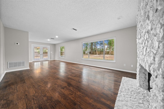 unfurnished living room with a stone fireplace, dark hardwood / wood-style floors, a textured ceiling, and french doors