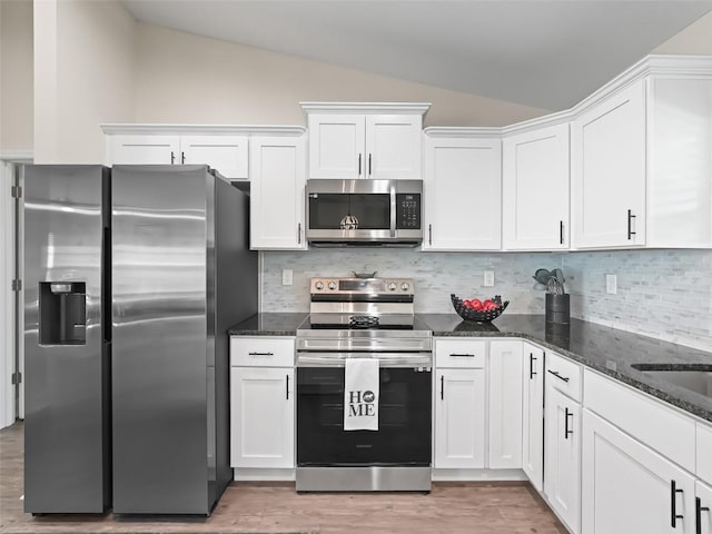 kitchen with white cabinetry, vaulted ceiling, stainless steel appliances, and dark stone counters