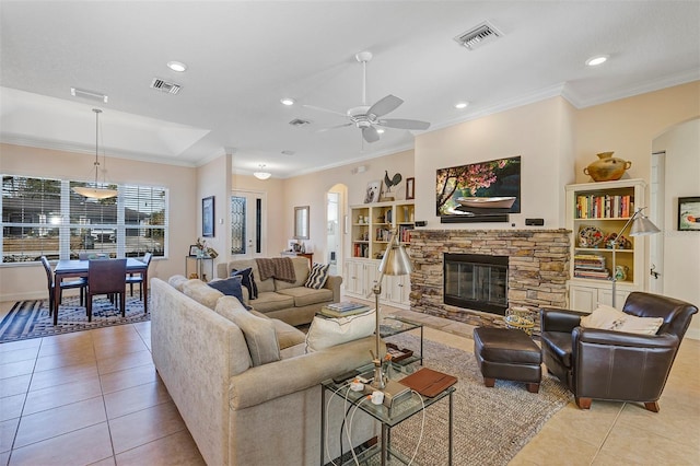 tiled living room with crown molding, a stone fireplace, and ceiling fan