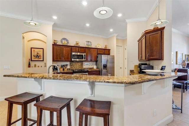 kitchen with crown molding, appliances with stainless steel finishes, decorative light fixtures, and a breakfast bar