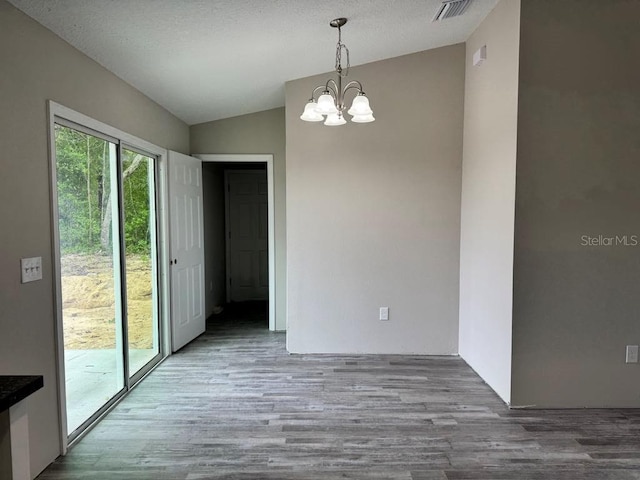 unfurnished dining area featuring lofted ceiling, a chandelier, and wood finished floors